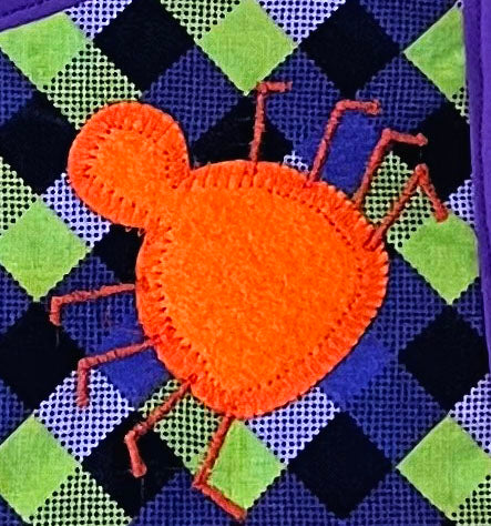 green and purple gingham bib with embroidered spider