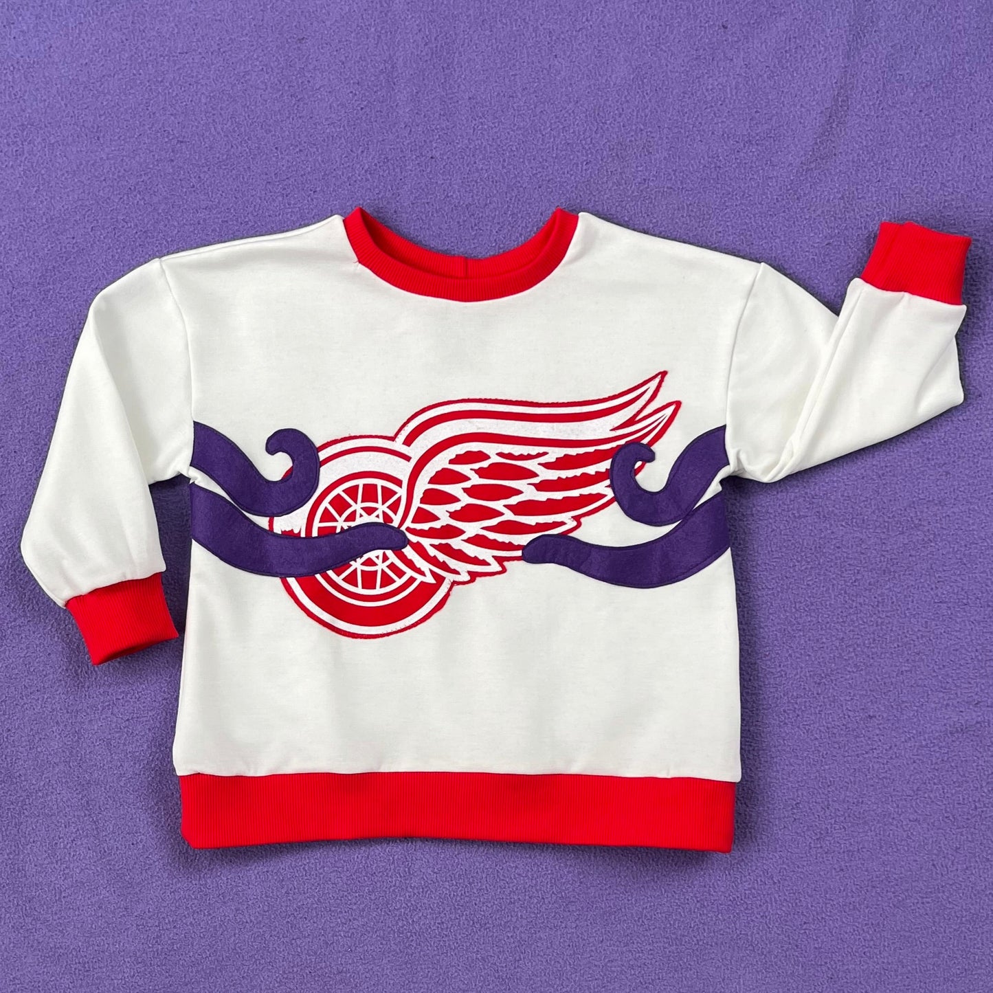 White sweatshirt with the Red Wings logo and four octopus tentacles sewn on, on a purple background