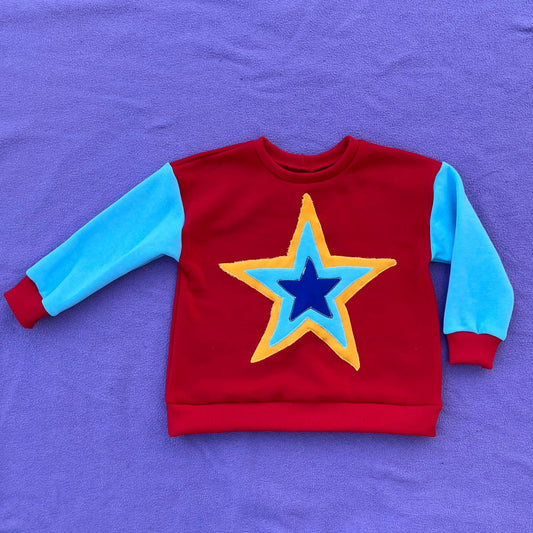 Red sweatshirt with a blue and yellow star and teal sleeves on a purple background
