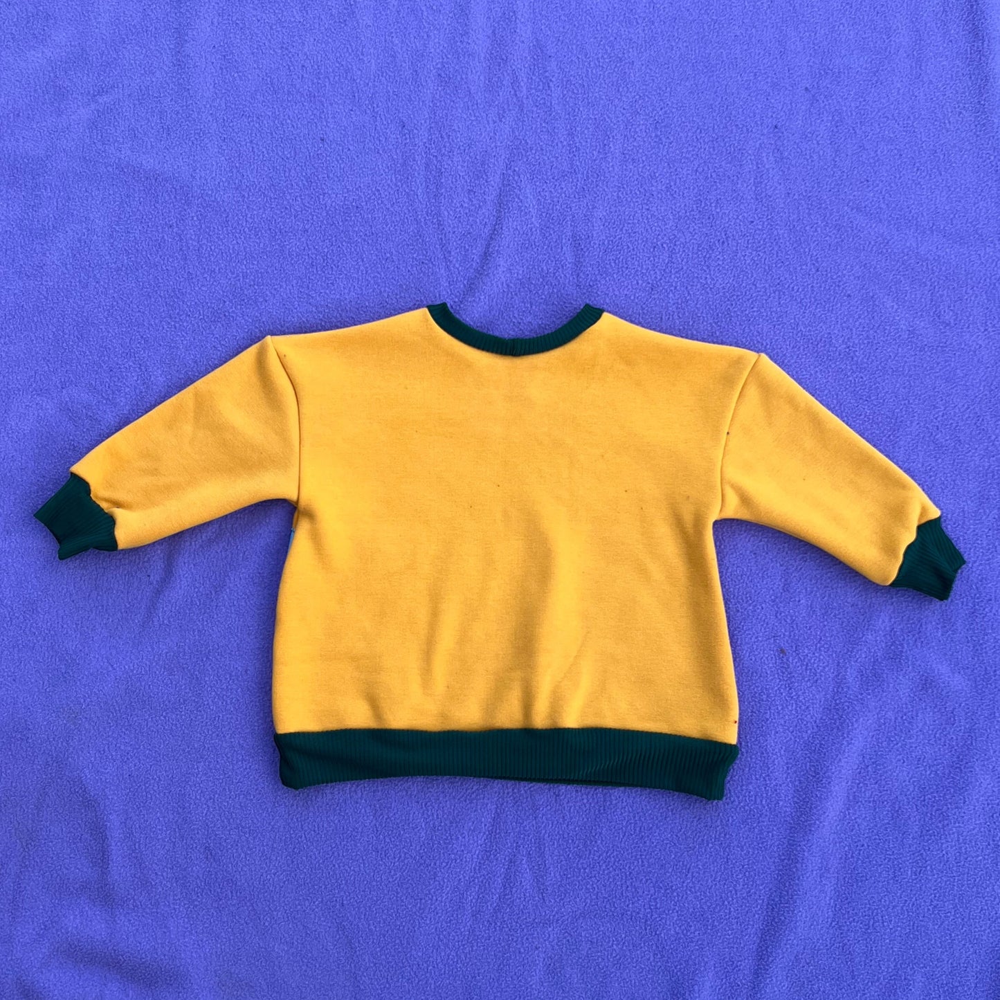 Yellow sweatshirt with green trim on a purple blanket