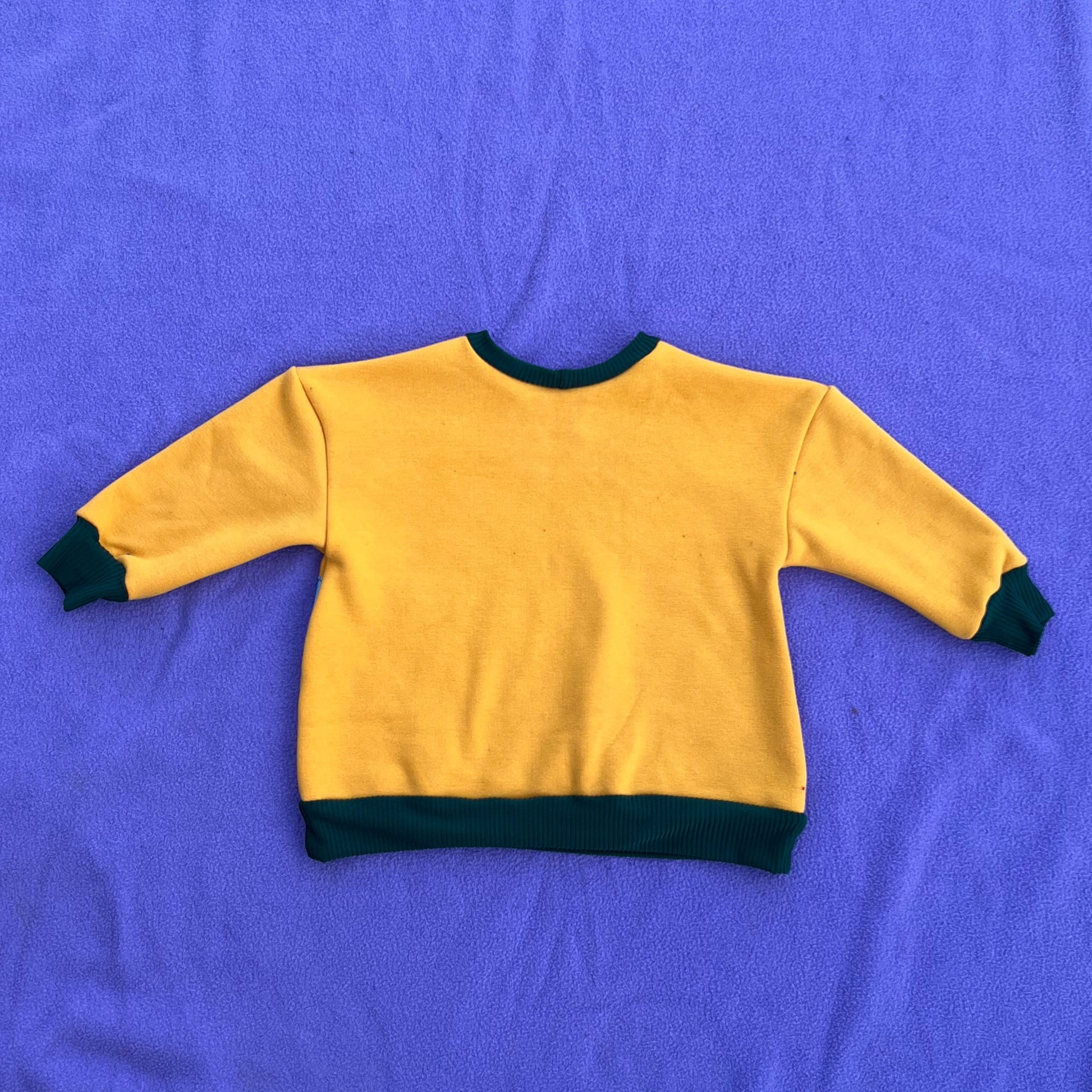 Yellow sweatshirt with green trim on a purple blanket