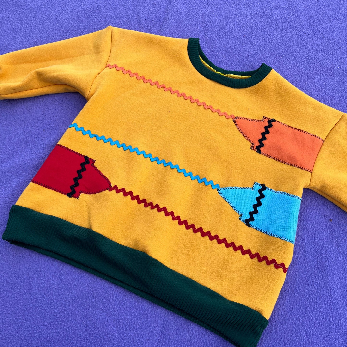 Yellow children's outfit with colorful crayon designs on a purple background