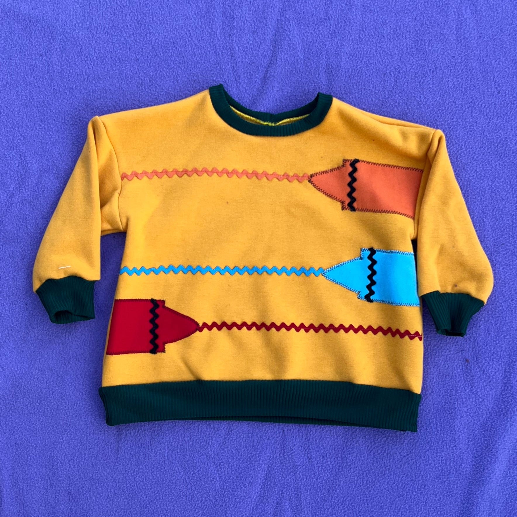 Yellow sweater with colorful crayon patterns on a purple background