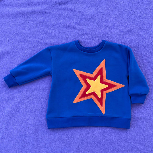 Blue sweatshirt with a red, orange, and yellow star design on a purple surface