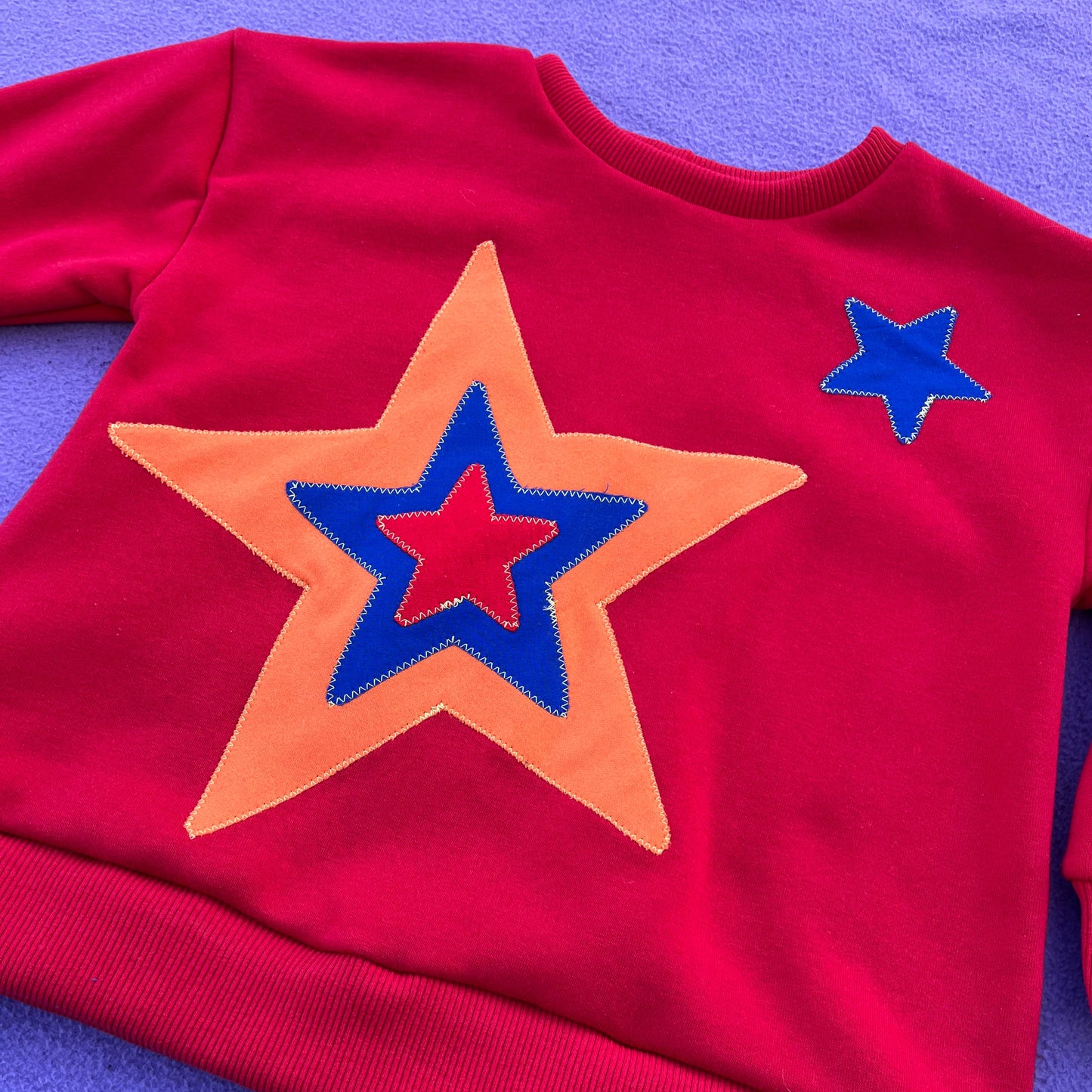 Red sweatshirt with red, blue, and orange star design on a purple background