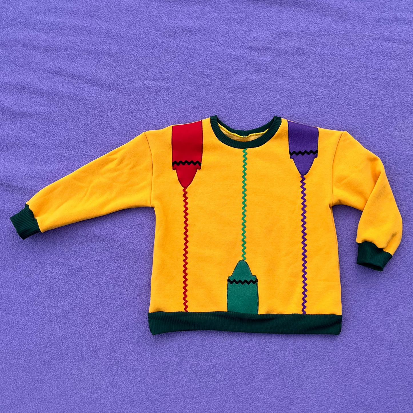 Yellow sweatshirt with a colorful crayon motif on a purple background.