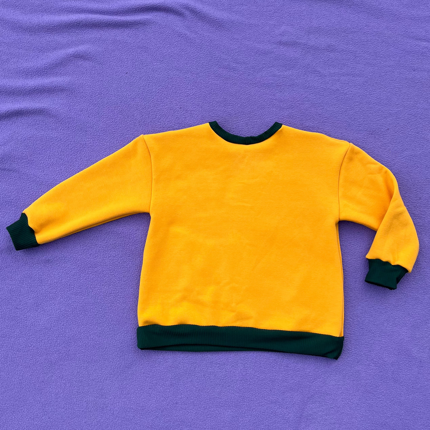 Yellow sweatshirt with green trim on a purple background.
