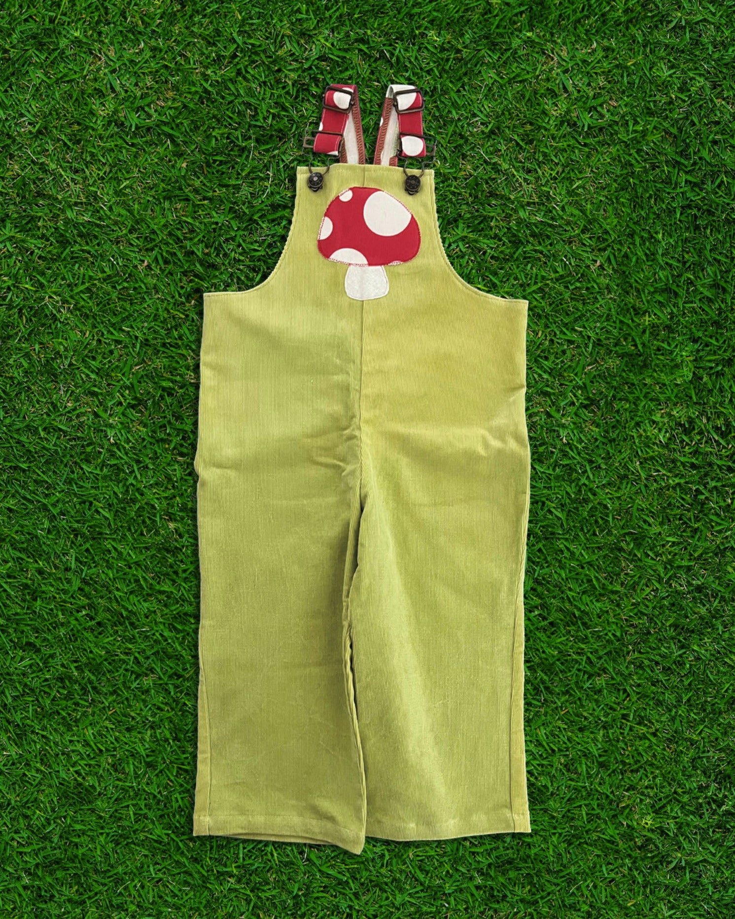 Green overalls with cartoon mushroom design on a green grass background