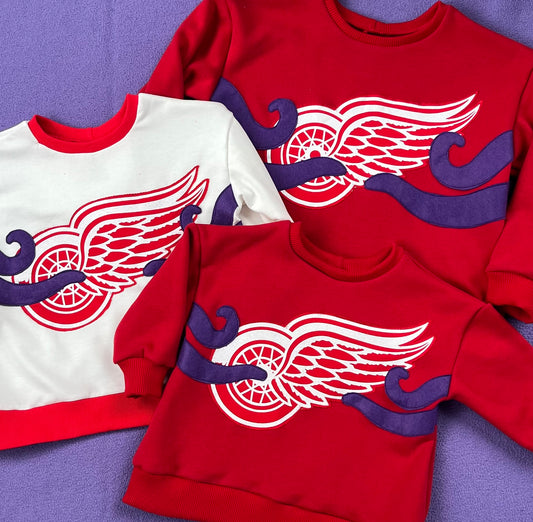 Three sweatshirts with a prominent Red Wings logo and purple tentacles on a purple background