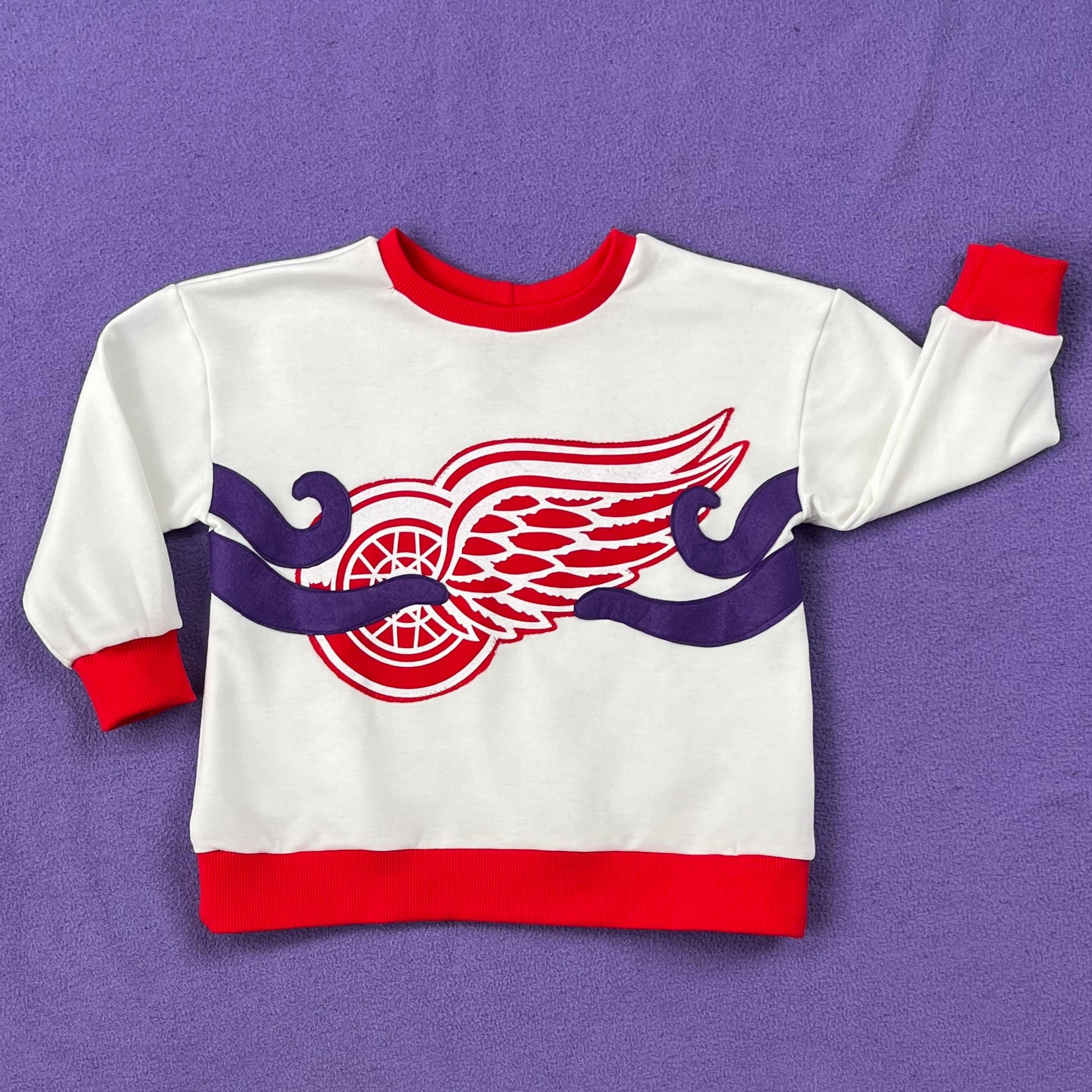 White sweatshirt with the Red Wings logo and four octopus tentacles sewn on, on a purple background